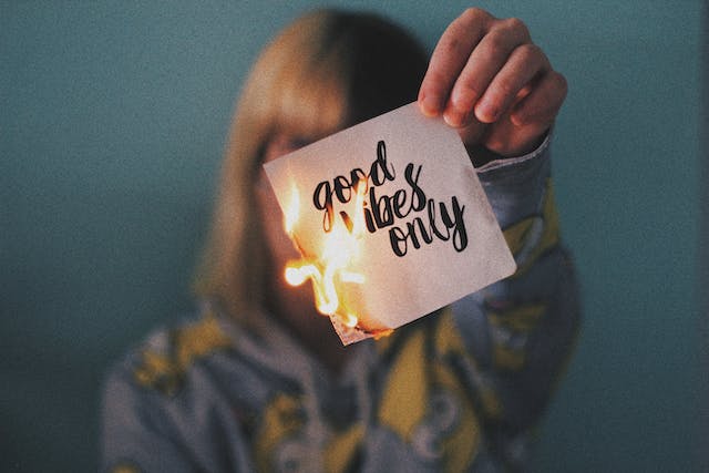 Frau hält brennenden Zettel in die Kamera, auf dem steht good vibes only